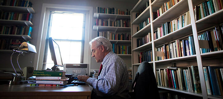 E. J. Dionne sitting at a computer, typing, with a bookshelf full of books behind him.
