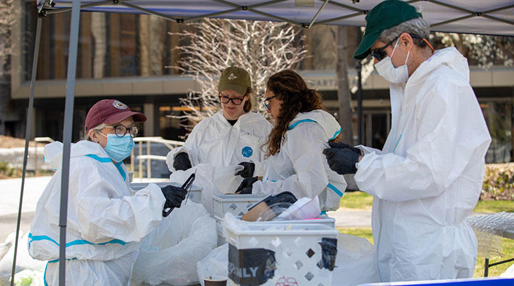 four people wearing white suits hold and analyze trash