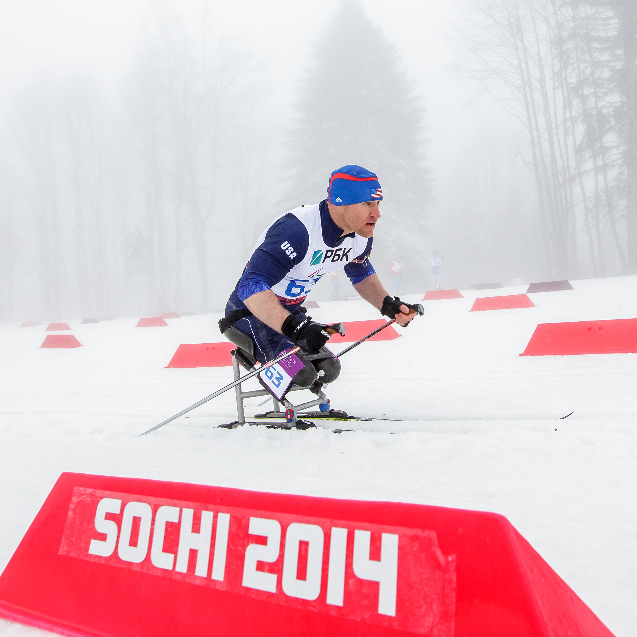 Dan Cnossen racing during the paralympic winter games, with a Sochi 2014 banner in the foreground.