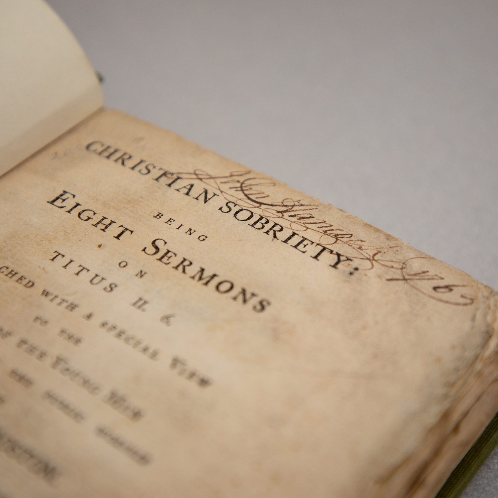 A historic book of sermons open to the cover page, at the top of which John Hancock's signature is written