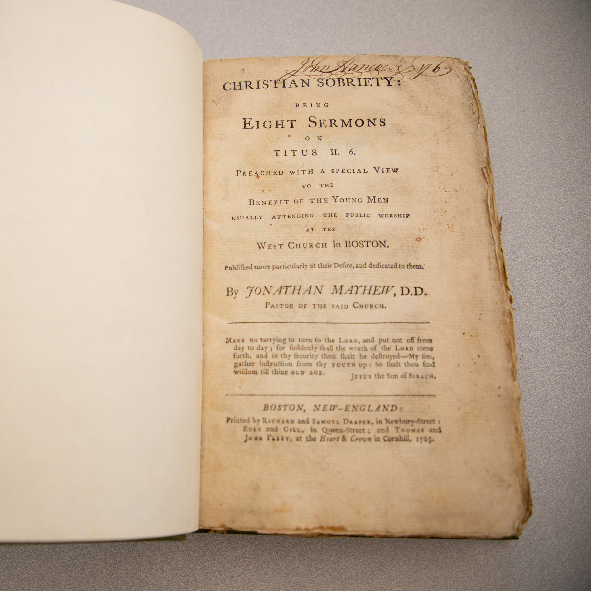 A historic book of sermons opened to the cover page, with John Hancock signature at the top of the page