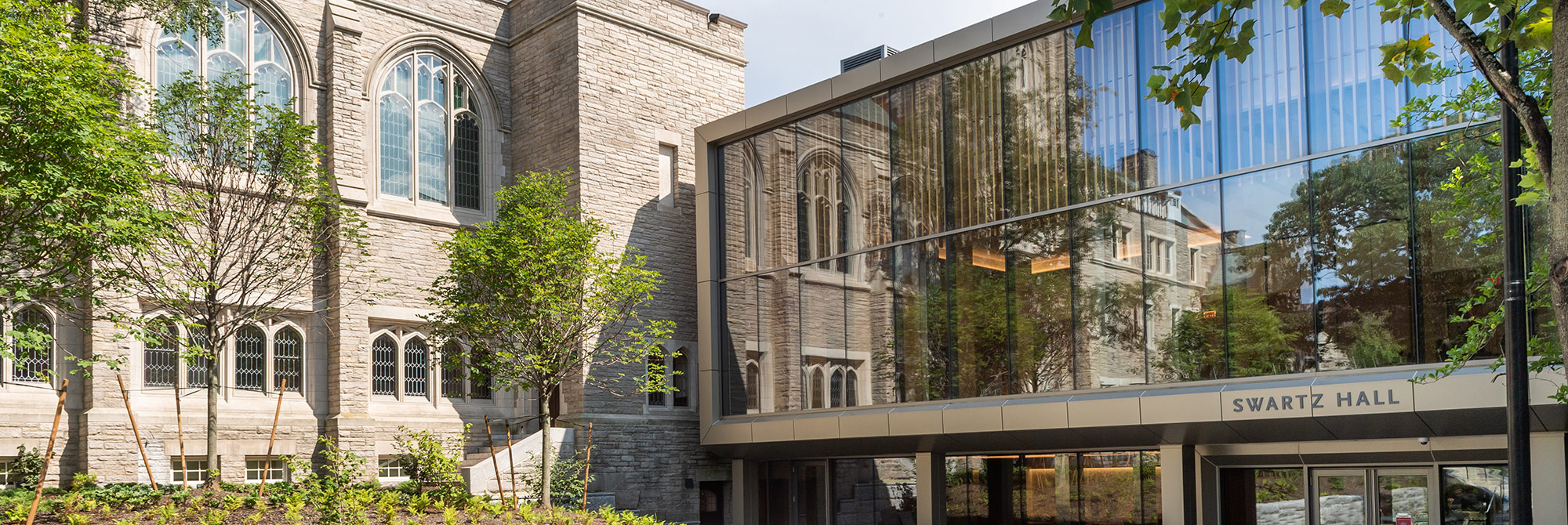 Swartz Hall entrance, with the old stone tower reflected in the windows of the new construction