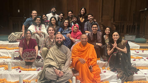 A group of students in variety of colorful outfits smile at the camera surrounded by candles and flower petals