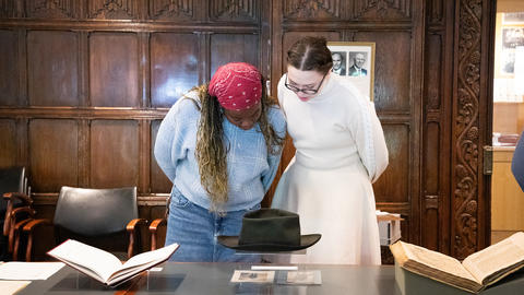 Two students looking manuscripts and a hat on display stands