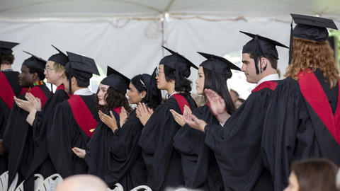 students in graduation caps and gowns stand in a line clapping