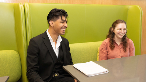 Two student sit in the HDS cafe laughing at something offscreen