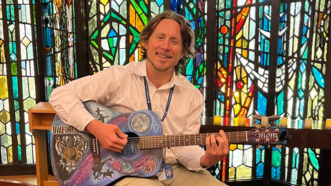 A student plays a colorful guitar against stained glass