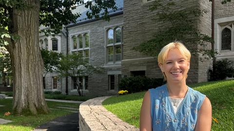 Lexi Potter sitting on stone with tree and Swartz Hall in background