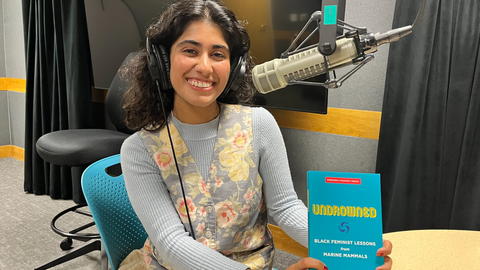 Mishka Banuri seated at a table with microphone to her right, holding a book