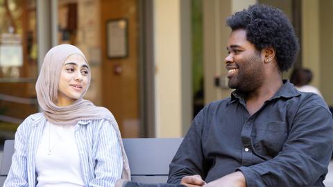 Two HDS students sit next to each other and smile, mid-conversation, in front of the main entrance to Swartz Hall.  