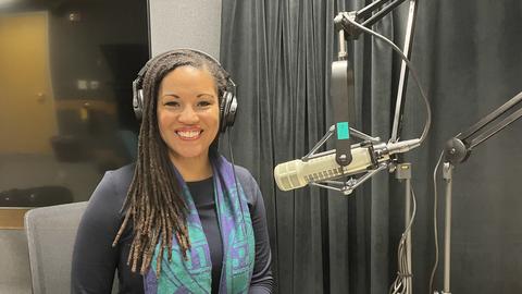 Michelle Millben sitting at a table wearing headphones with a microphone in front of her