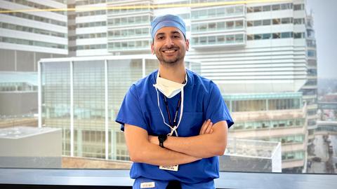 Danish Zaidi in blue scrubs posing by a window