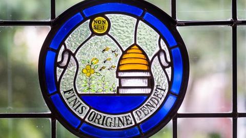 Stained Glass showing beehive with Latin text banner, 'finis origine pendet'.