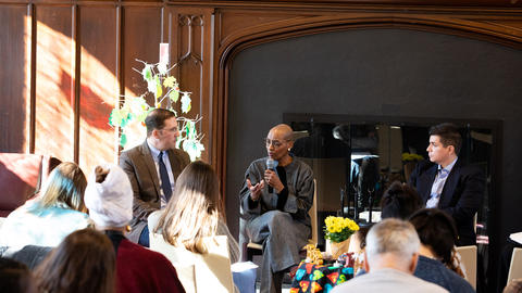 David Holland, Kelly Brown Douglas, and Raul Zegarra sit side-by-side during a conversation, with brown wall behind them and sunlight coming in on the left side