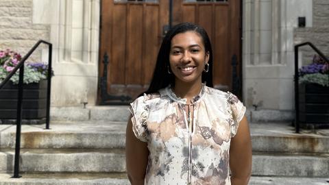 Janeen Green, MTS '26, stand smiling before the entrance to Swartz Hall on he HDS Campus