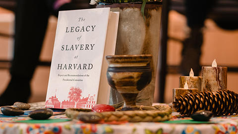 The Harvard Legacy of Slavery report book sits on a table surrounded by flowers, candles, and other decorative pieces