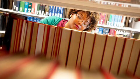 A student scans the titles of books on a library shelf.