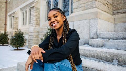 Aliyah Collins sits on the steps of Swartz Hall looking at the camera.