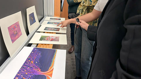 Students point at multiple pieces of artwork on display on a ledge