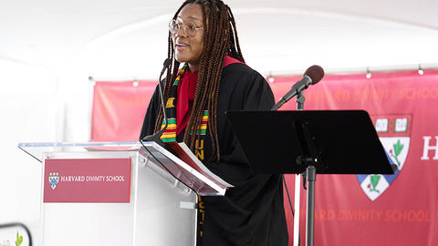 Breana Norris speaking at a clear podium wearing an academic robe