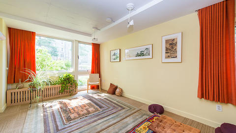 Small sunny room with plants, pillows, small stools, and rugs