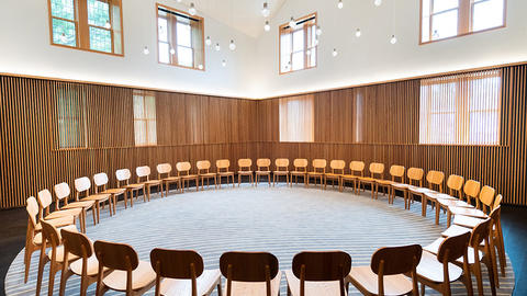 Spacious, sunny room with high ceilings, wooden paneling, hanging glass globe lights, and a circle of chairs