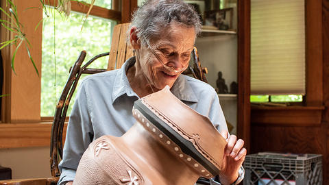 Ramona Peters holding and looking at a brown clay pot with white inlay gliphs