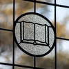 Photo of stained glass window showing an open book, with autumn leaves showing through the glass