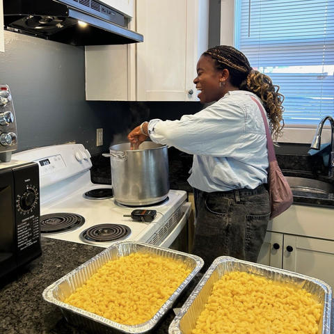 Sarah Adegbite in front of a stove with two pans of pasta in the foreground
