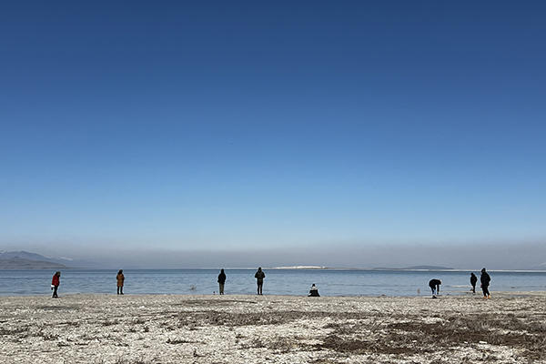 Landscape portrait with blue sky, a lake in the distance, and figures standing on the shore