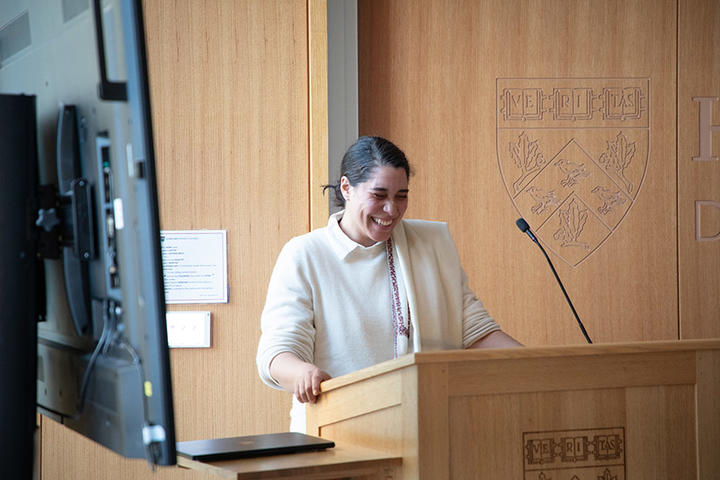 a person stands behind a lectern with a screen to the left of the image