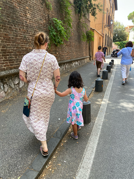 Amy Sexauer wears a long dress and walks down the street with her daughter. Their backs are to the camera