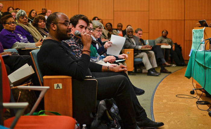 A student speaks into a microphone in a crowded lecture hall