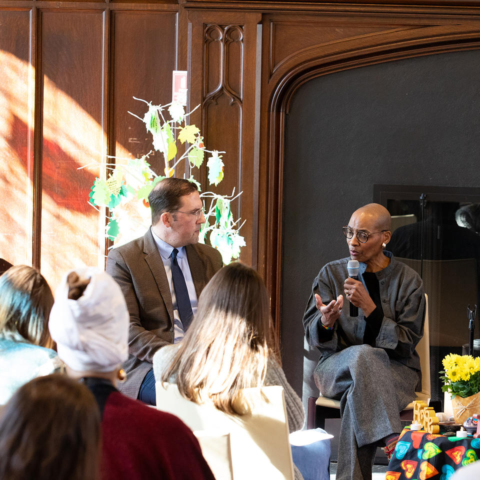 David Holland, Kelly Brown Douglas, and Raul Zegarra sit side-by-side during a conversation, with brown wall behind them and sunlight coming in on the left side