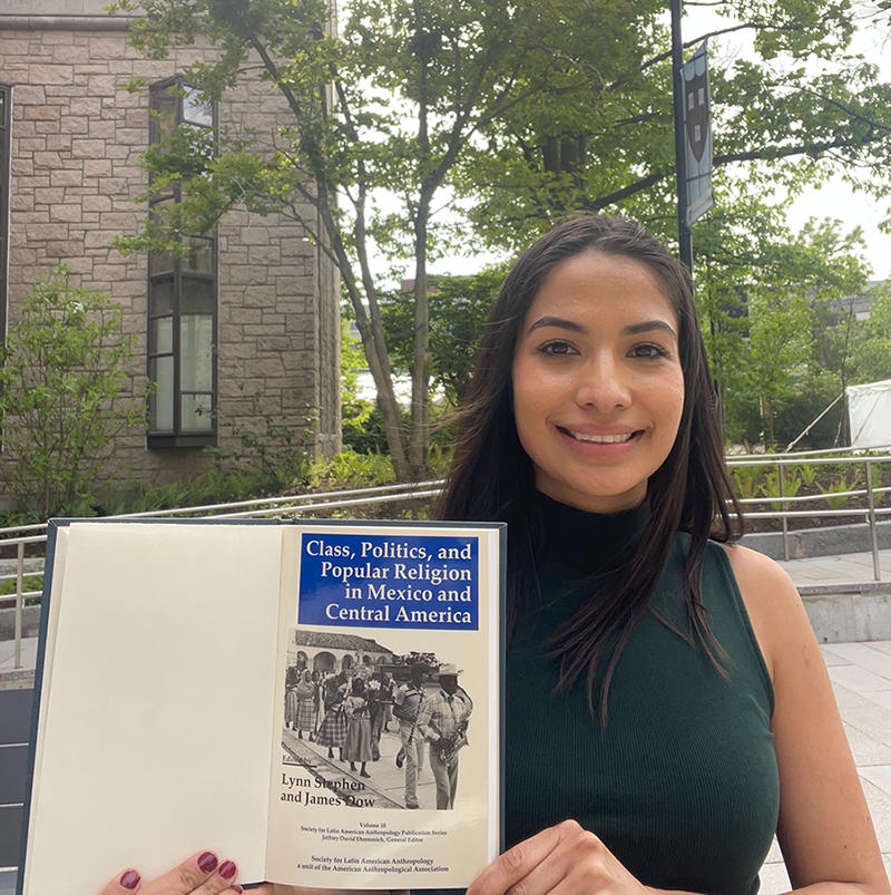 Maria Dueñas Lopez sits outside Swartz Hall holding up a book