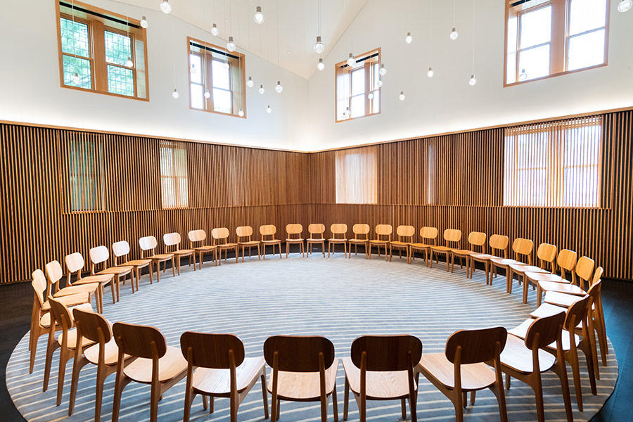 Spacious, sunny room with high ceilings, wooden paneling, hanging glass globe lights, and a circle of chairs