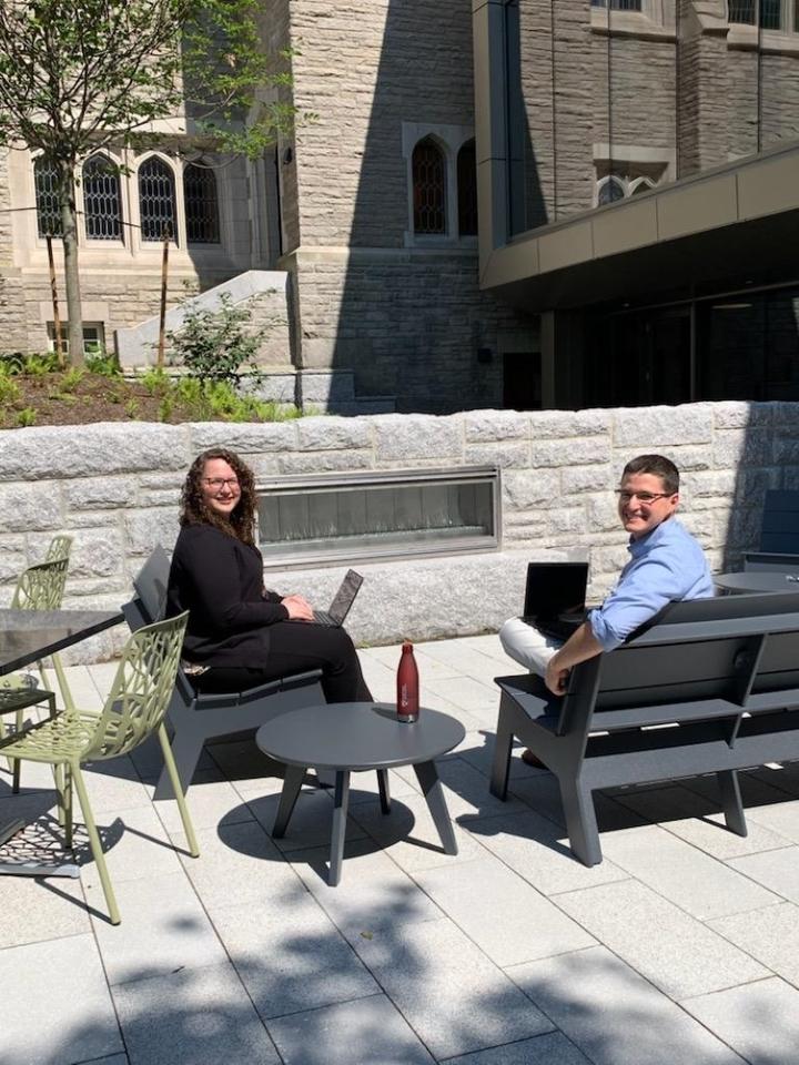 Two people sitting outside looking at the camera near entrance to Swartz Hall