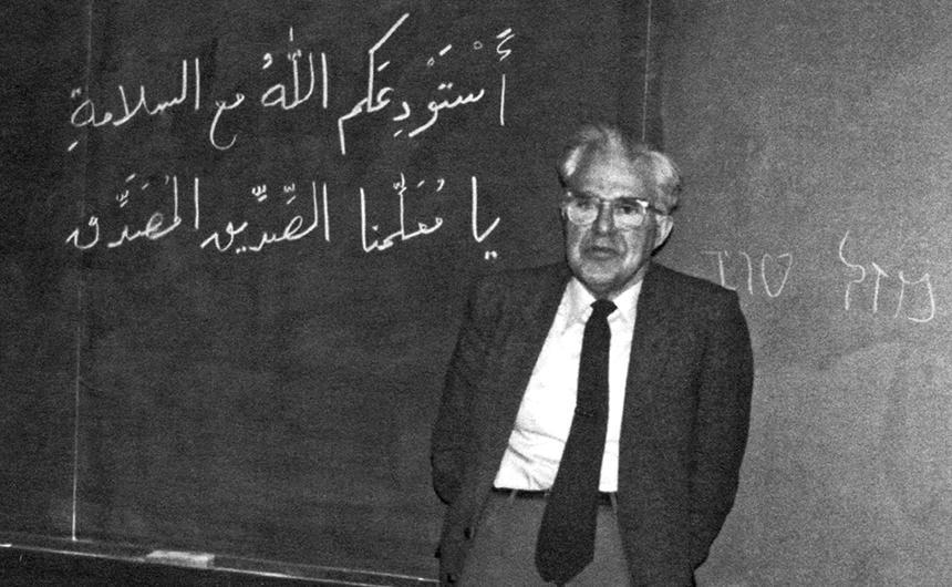 Wilfred Cantwell Smith standing in front of a chalkboard with Arabaic text written on it