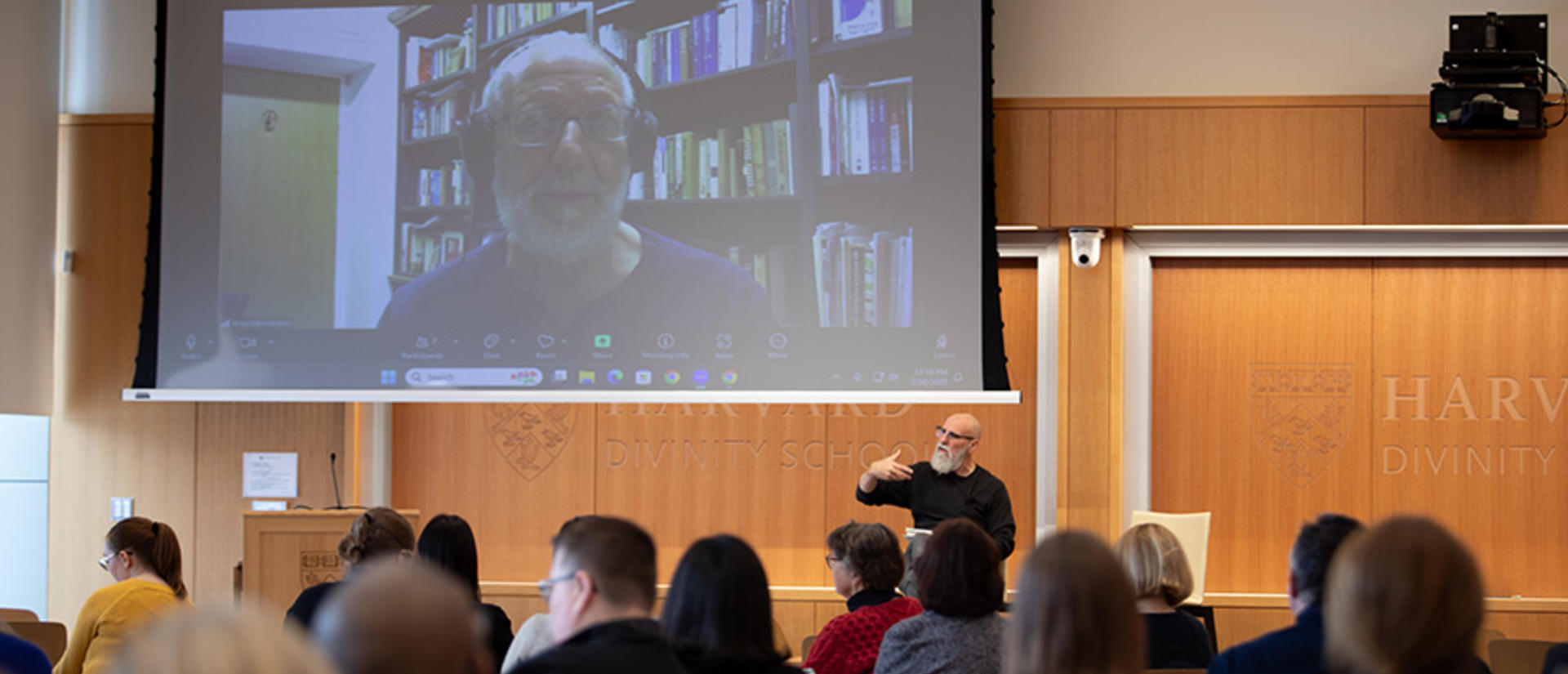 man in center before audience speaks virtually with guest on screen to man's left