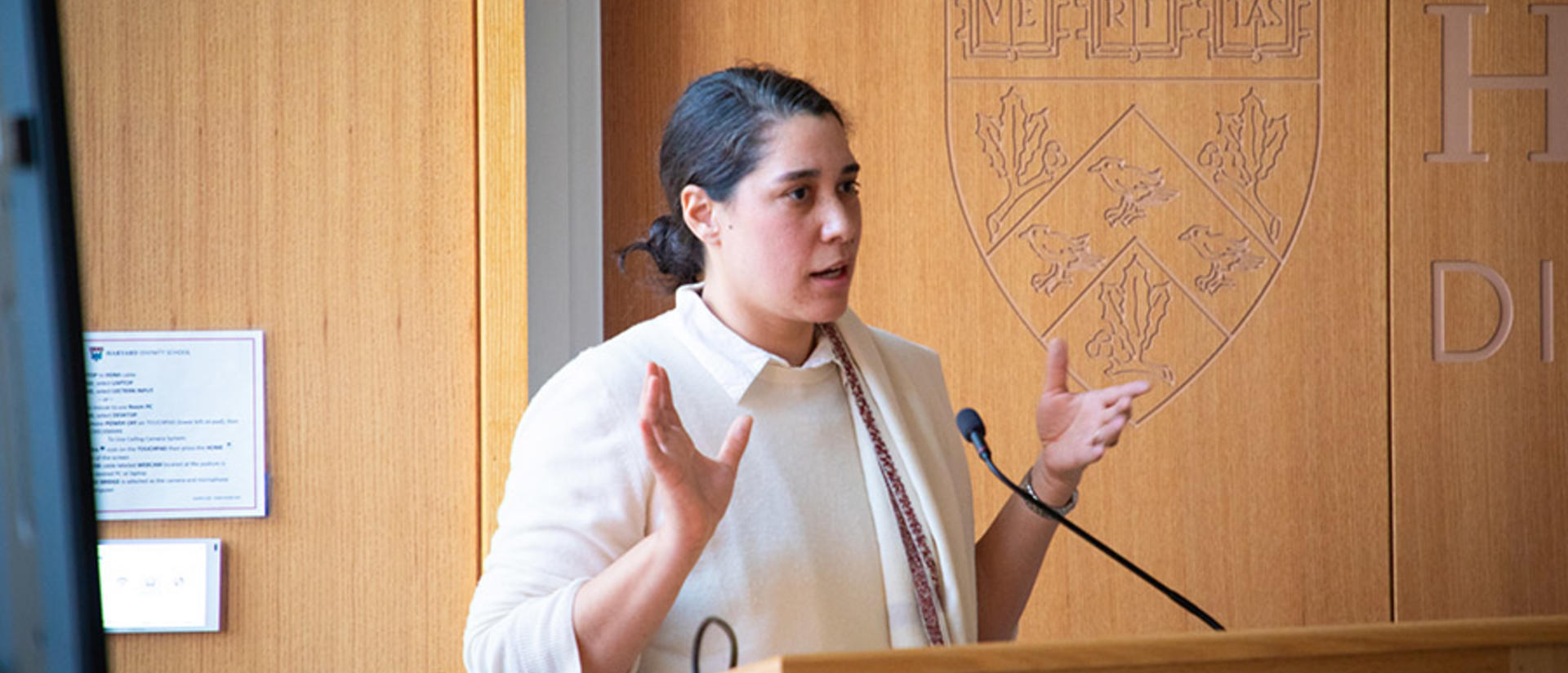 person speaks behind a lectern with a wood backdrop behind them