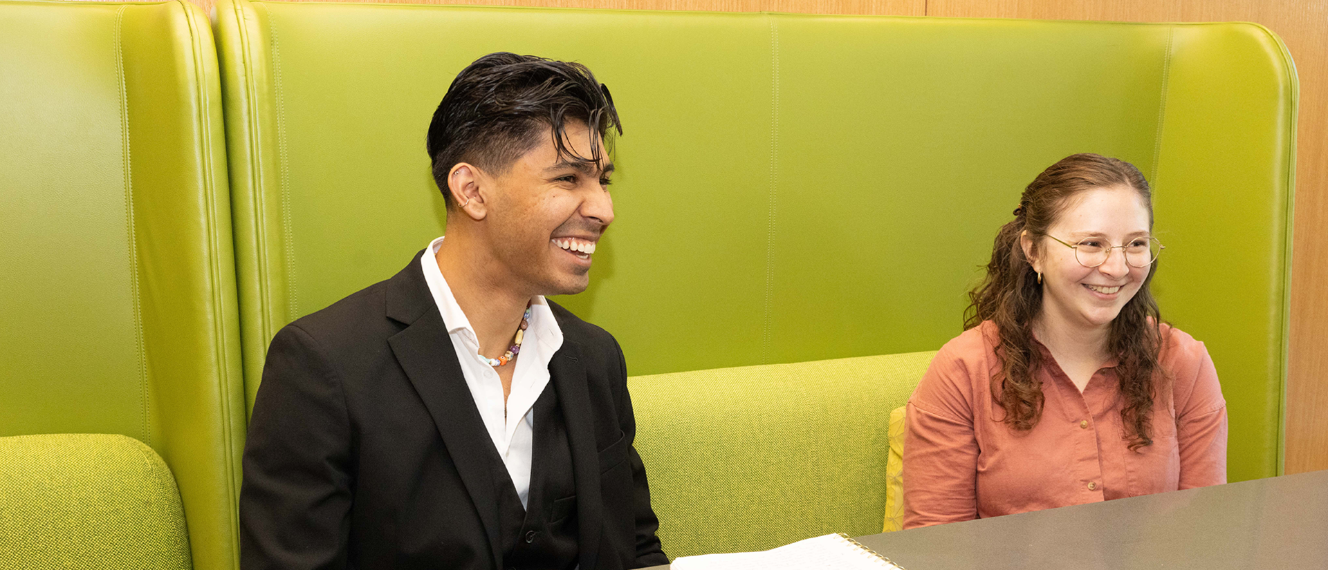 Two student sit in the HDS cafe laughing at something offscreen