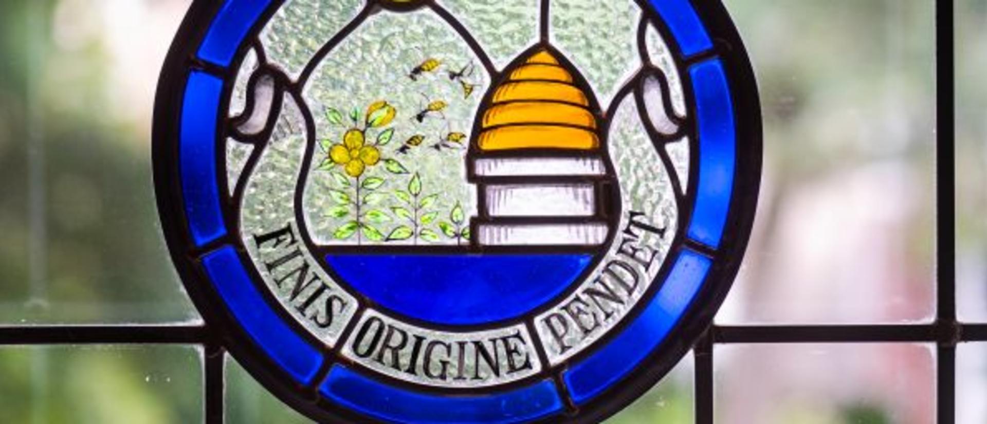 Stained Glass showing beehive with Latin text banner, 'finis origine pendet'.