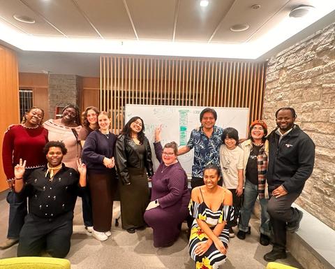 A group of students and leaders point to a fundraising poster